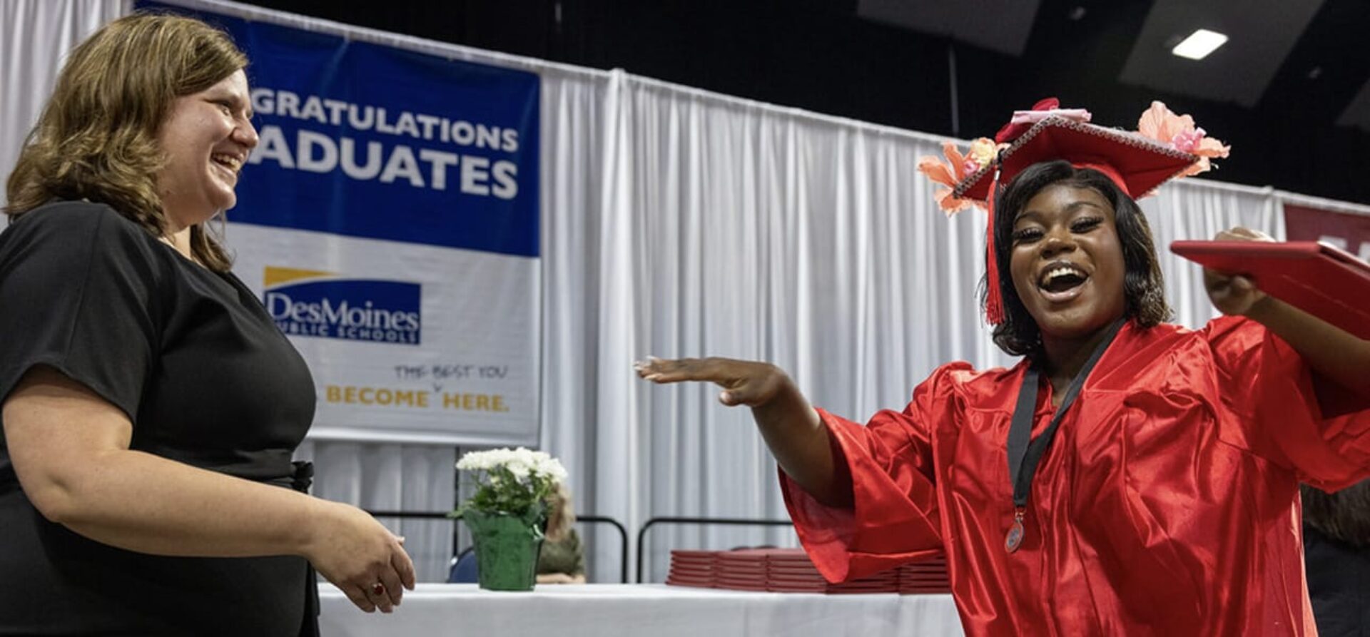 A female student dressed in a red graduation cap and gown smiles as she accepts her diploma