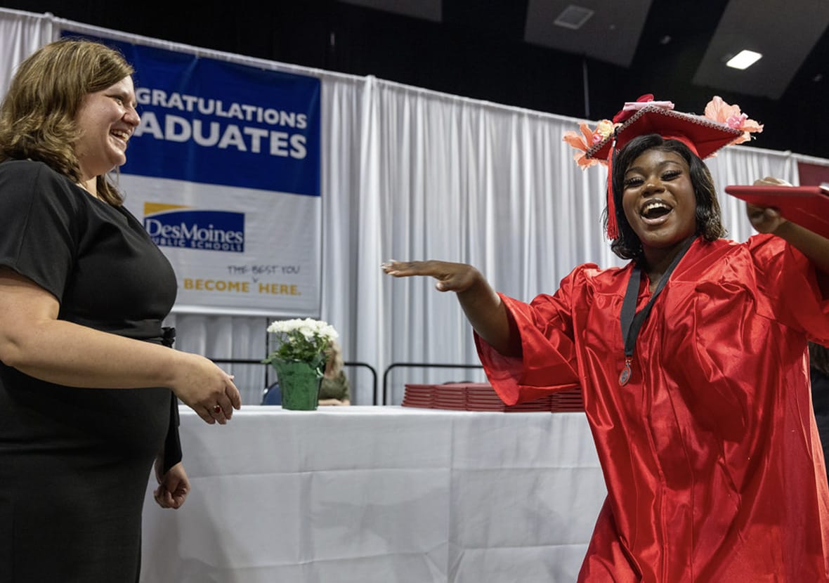 A female student dressed in a red graduation cap and gown smiles as she accepts her diploma